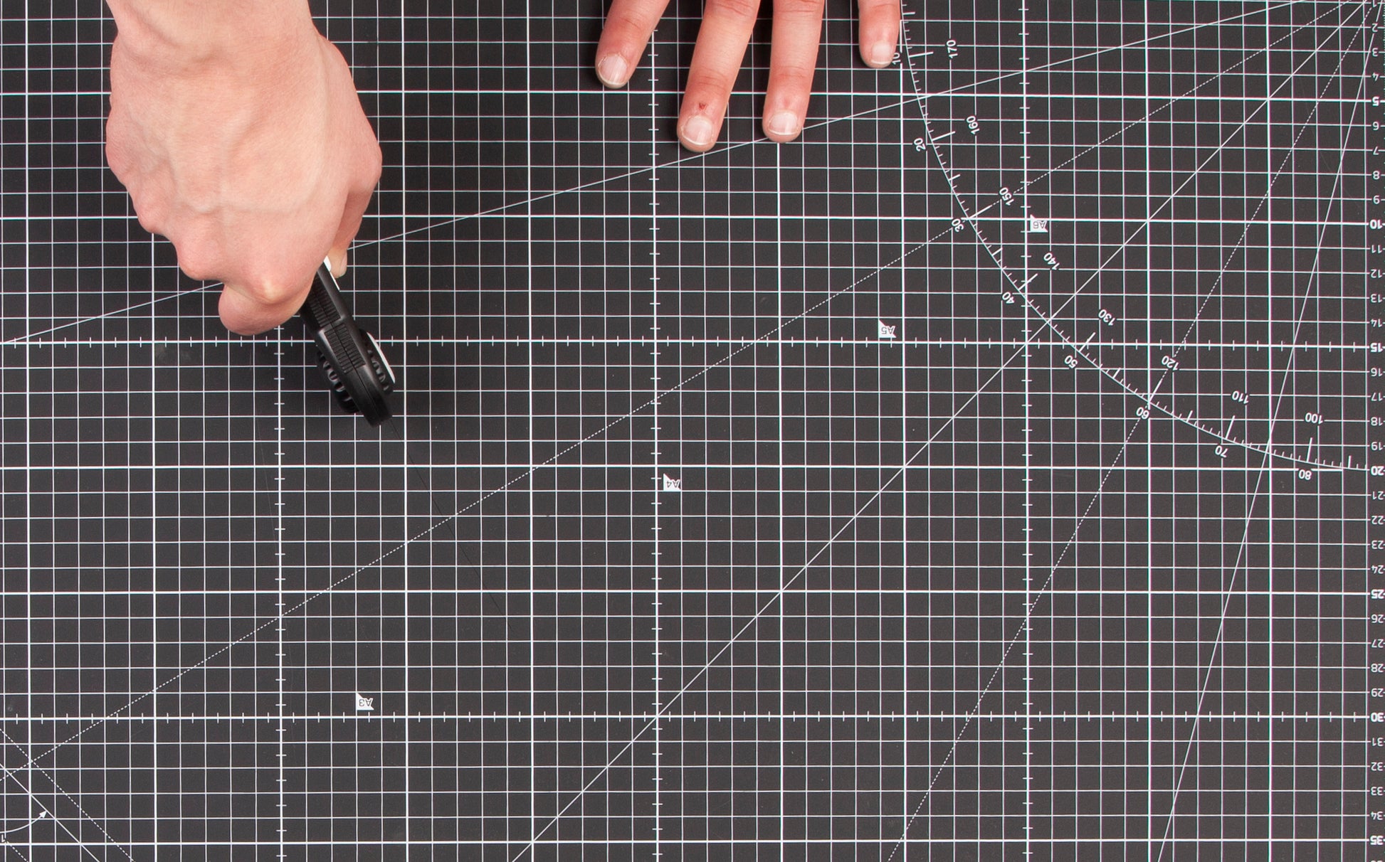A guy using a rotary cutter on the black cutting mat in overview. 